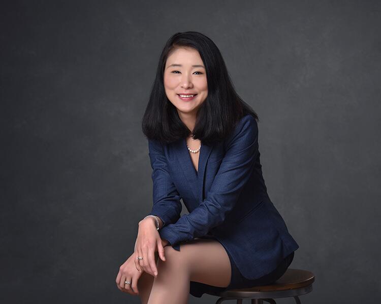 Jingze Jiang, wearing a navy blazer, seated against a gray studio background